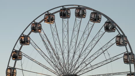 Silhouette-Of-People-Inside-Glass-Cabins-Of-A-Ferris-Wheel-Gently-Spinning-Against-Clear-Sky-On-A-Sunset---low-angle,-medium-shot