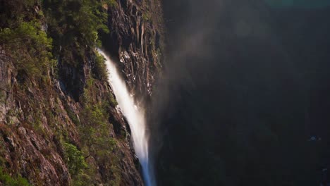 static view of ellenborough falls in australia, water flowing off the cliff edge with haze and mist lit by golden hour light