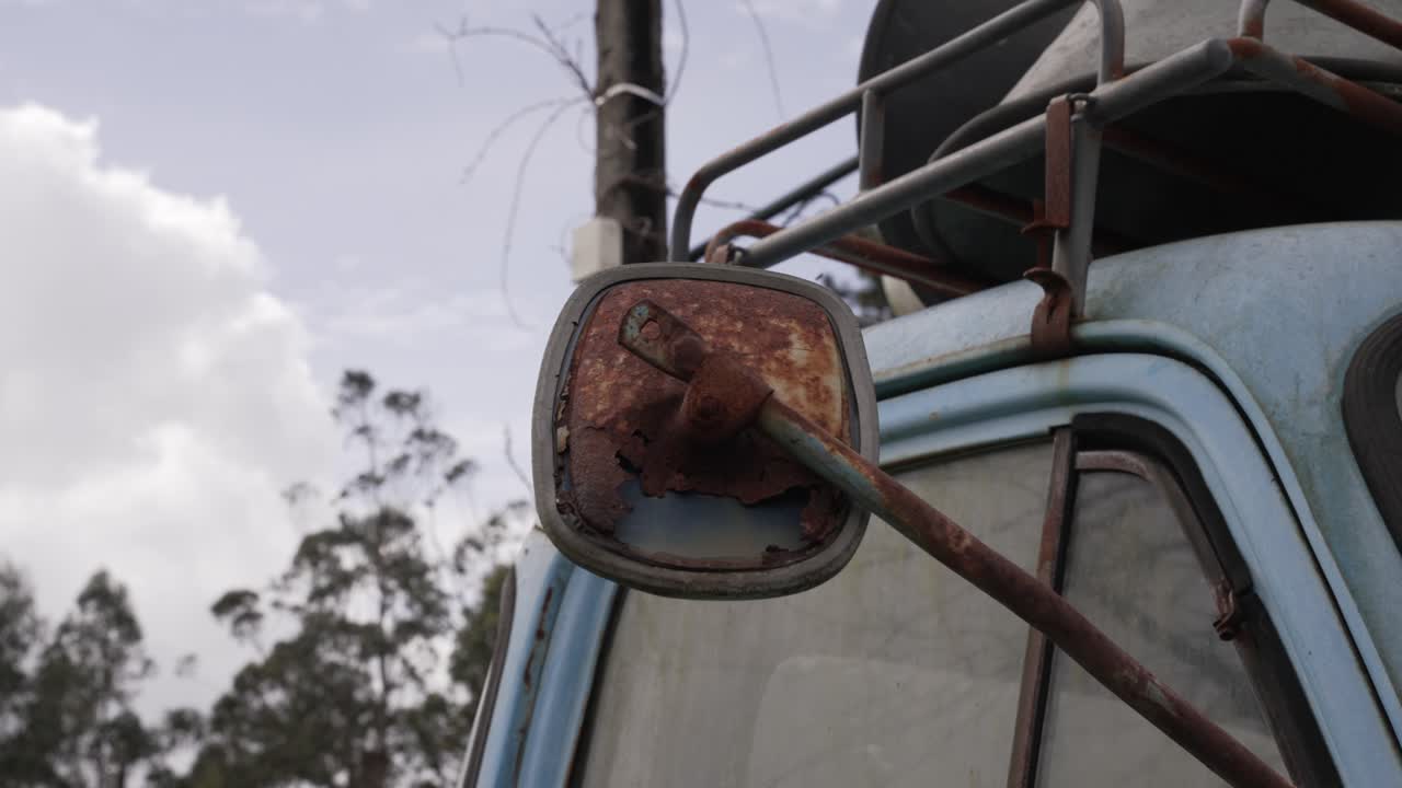 Close up of a heavily rusted side mirror on a faded blue vintage truck