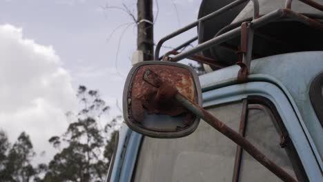 close up of a heavily rusted side mirror on a faded blue vintage truck