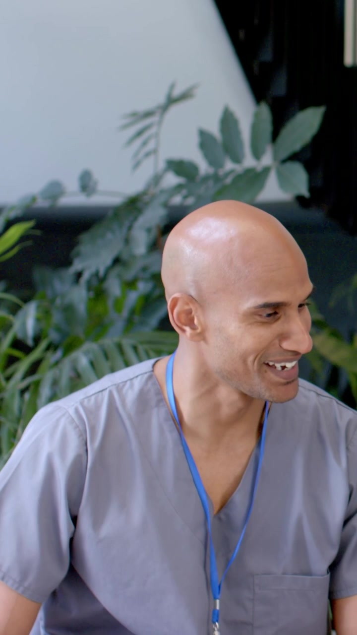 Vertical video: On cue, man in gray scrubs turning toward voice, smiling in lounge, blue lanyard ID