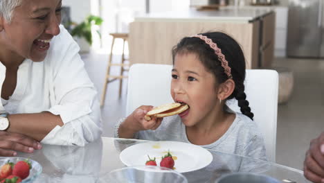 biracial granddaughter enjoys a waffle, biracial grandmother watches with joy