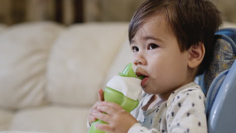 a baby of two years drinks milk from his bottle, sits on a high chair