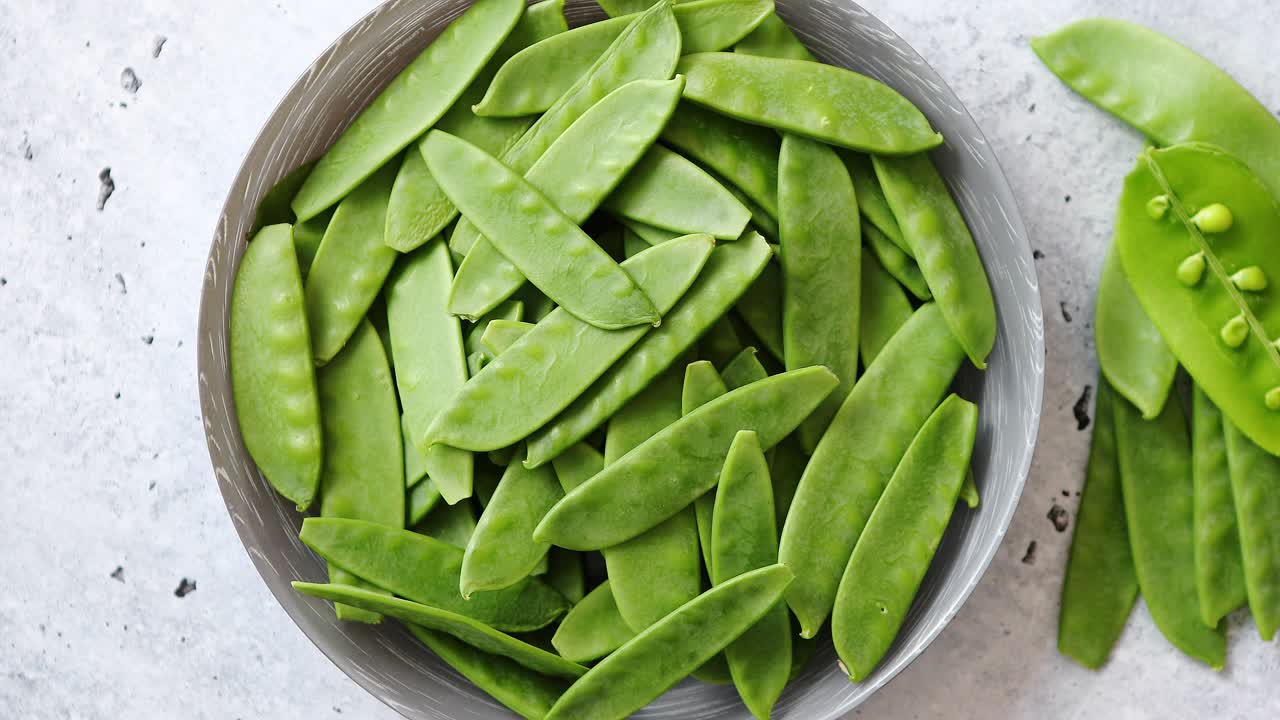 Fresh green peas in white ceramic bowl on gray stone background
