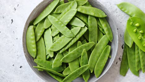 Fresh-green-peas-in-white-ceramic-bowl-on-gray-stone-background