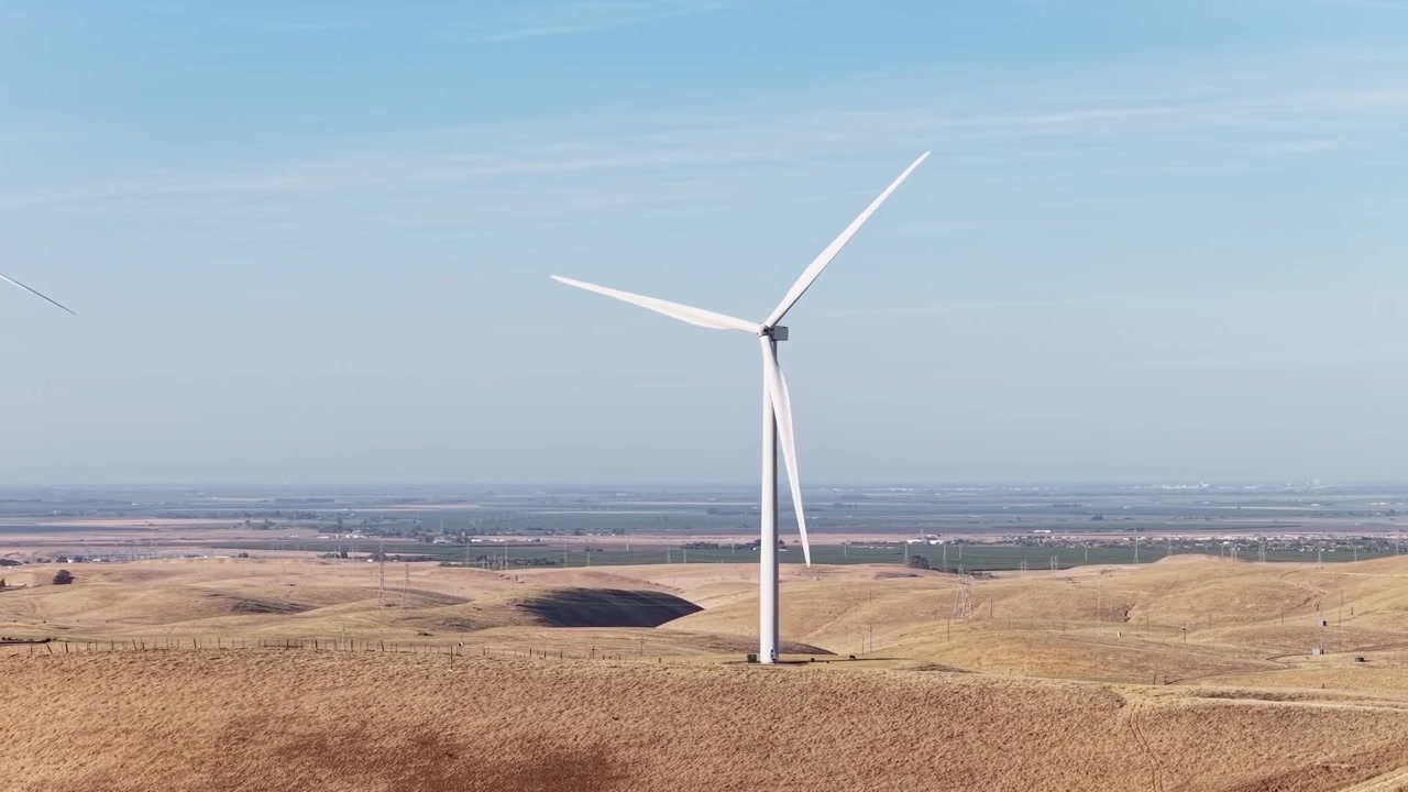 Turbine eoliche che girano nella brezza sulle dolci colline dell'Altamont Pass nella California settentrionale, generando energia pulita e rinnovabile sotto un cielo azzurro e limpido in una giornata di sole.