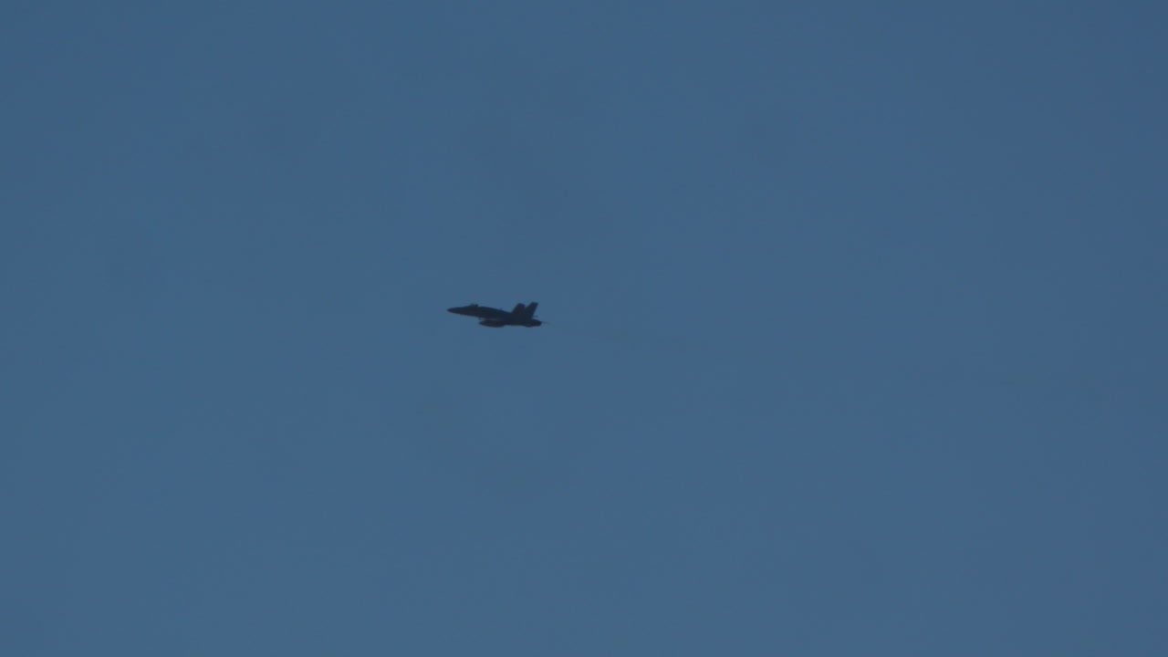 Silhouette of a Military Jet Flying Across a Clear Blue Sky