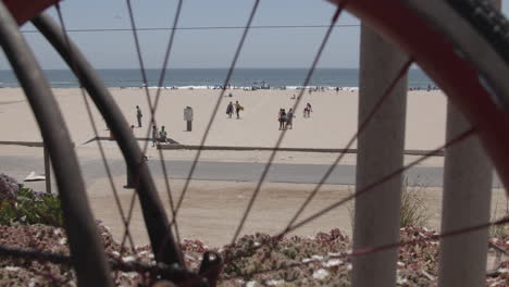 people enjoying the summer beach season in california as seen through the wheel of a bicycle slowing zooming out