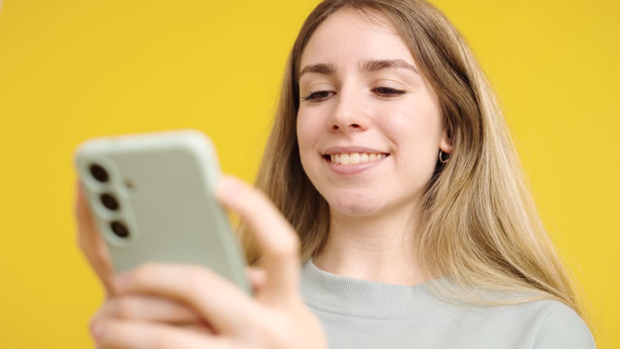 Young woman using smartphone on yellow background