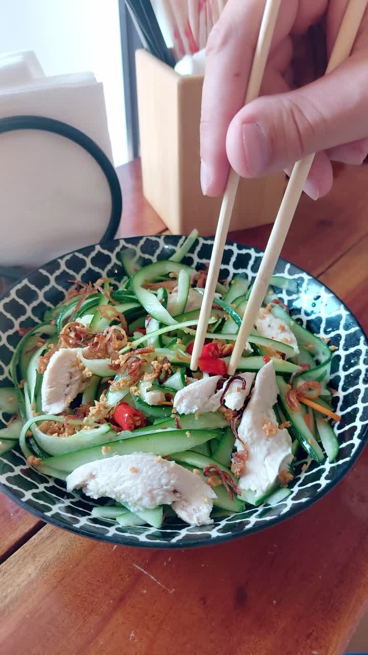 Close up to a plate of thit ga goi tom or traditional Vietnamese chicken cucumber salad with red chili being eaten, candid moment of experiencing local cuisine of Vietnam