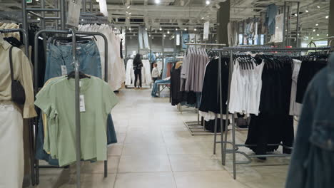 first-person view of a clothing store showcasing a variety of clothes on racks, including shirts, jackets, and jeans. a lady and a little boy are seen shopping in the store