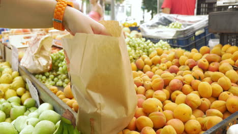 un comprador poniendo albaricoques en una bolsa de papel