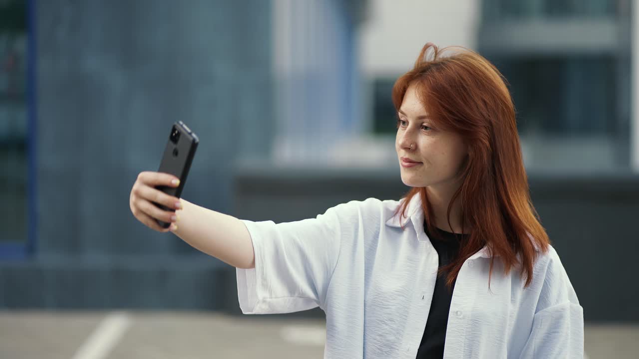chica pelirroja en una camisa hace una selfie en un fondo de la ciudad