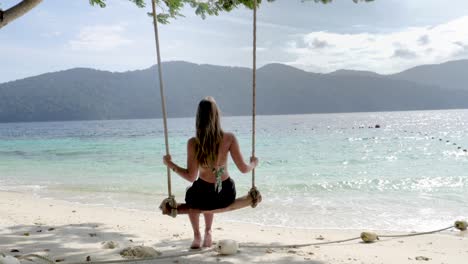 ultra slow motion shot of young caucasian woman sitting on swing on beautiful beach on island in thailand