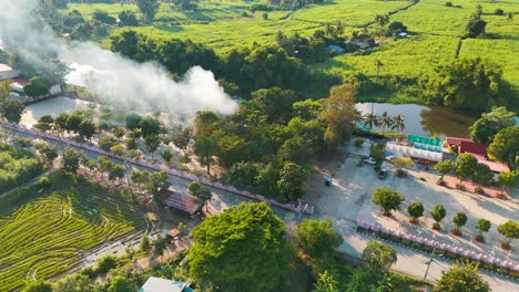 small fire and smoke plume next to a rural village and temple in thailand
