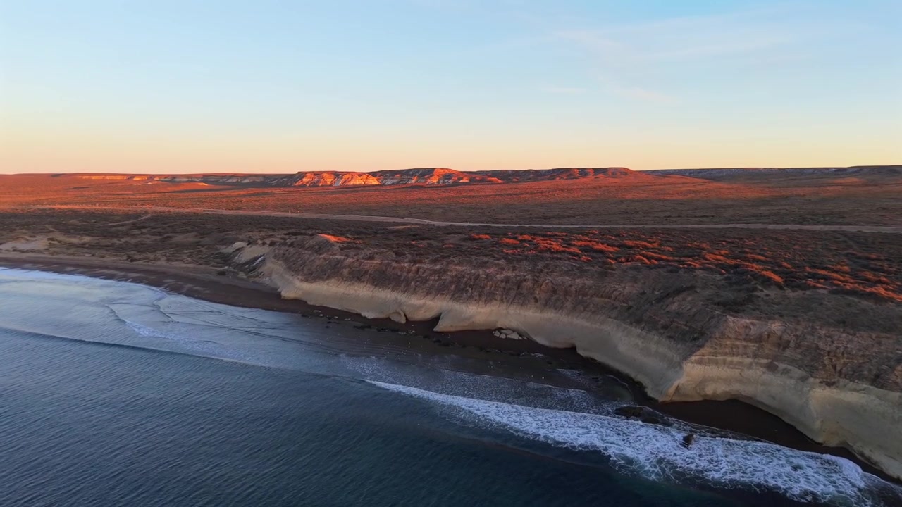 Soloppgang over rolig havvann med mykt lys langs Puerto Madryn-kystlinjen i Patagonia, droneoversikt.