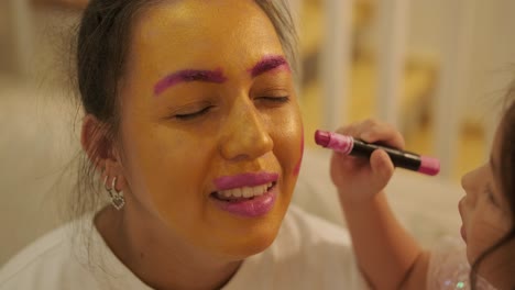 little girl applying makeup to her pregnant mother at home