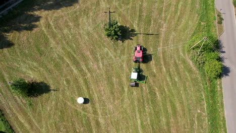 agriculture machinery in green field, tractor and hay bales machine rotating in agricultural farmland, aerial top down view of farm agricultural work