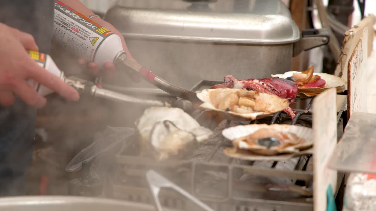 Close-up shot of a vendor using a blowtorch to grill scallops and oysters in Tokyo