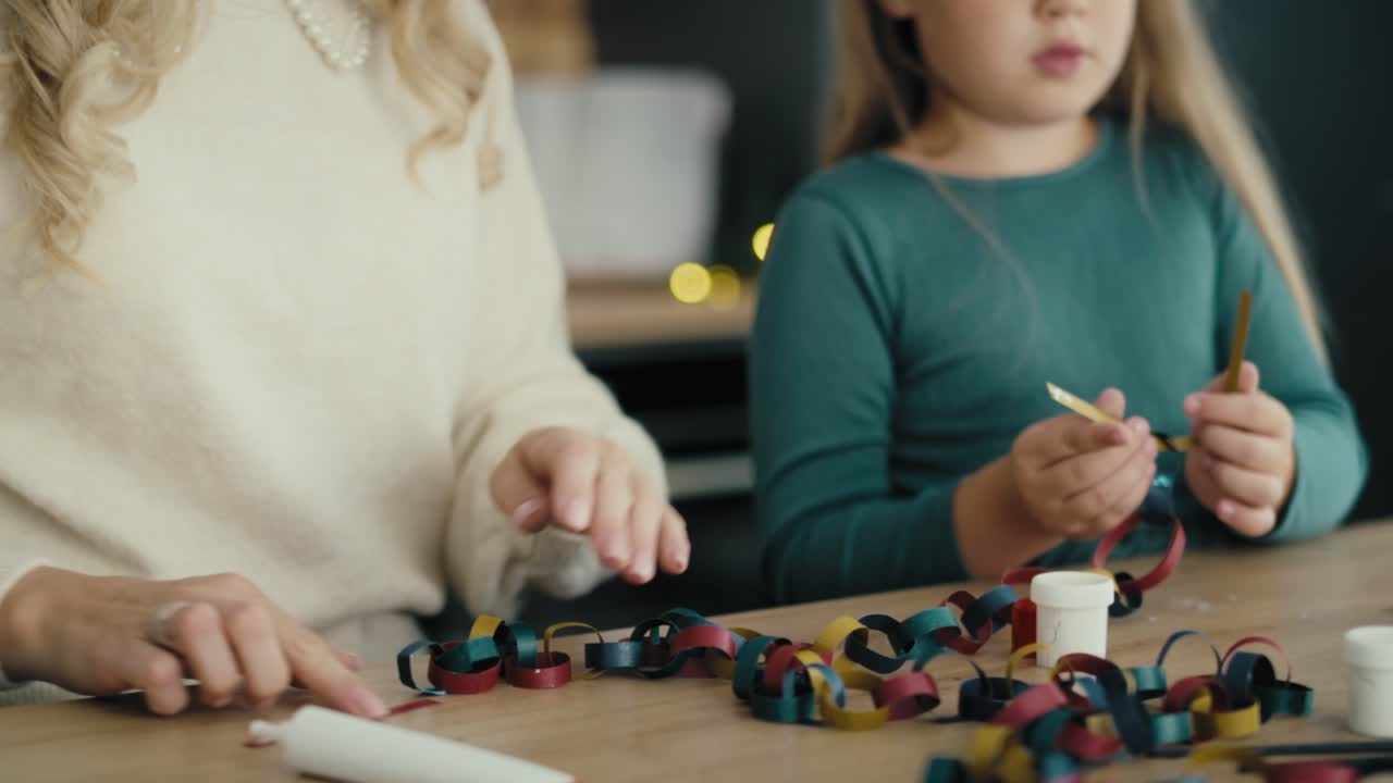 niña caucásica y madre preparando una cadena de papel para el árbol de navidad y hablando.