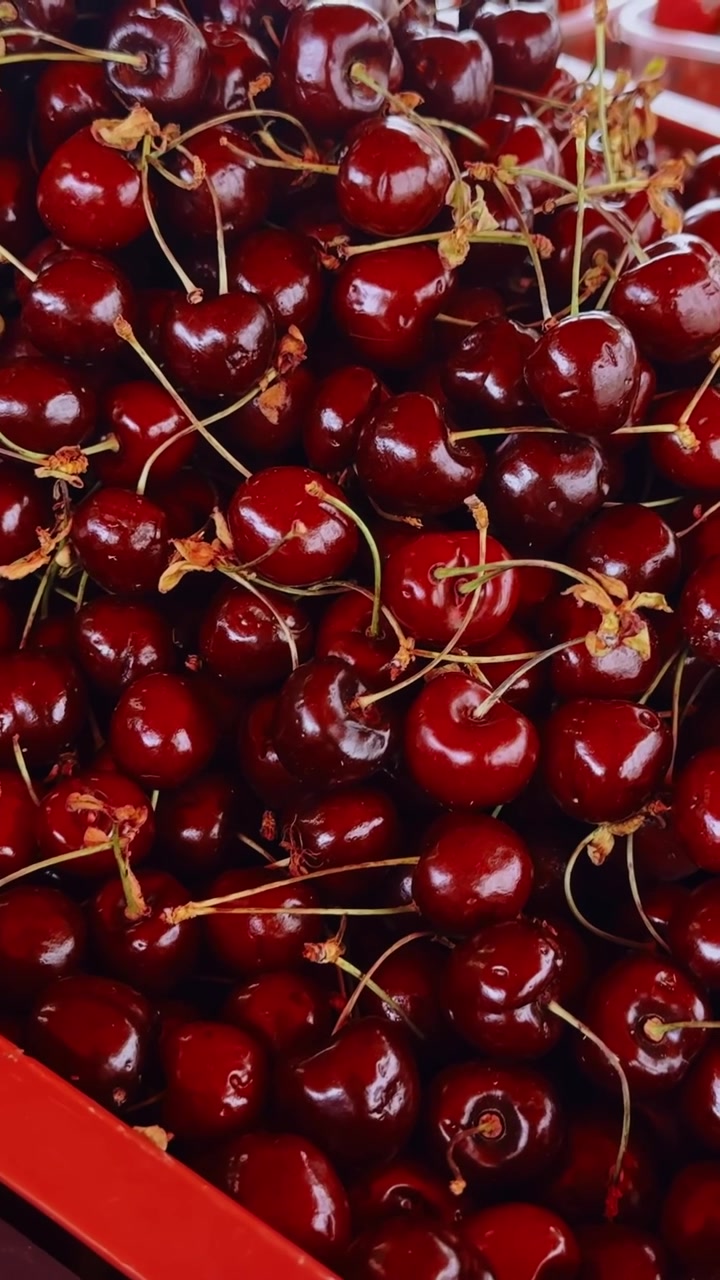 Primo piano di ciliegie rosse mature ammassate in cassette da mercato, che mostrano bucce lucide, gambi e un ricco colore naturale in un'esposizione di cibo fresco di stagione.