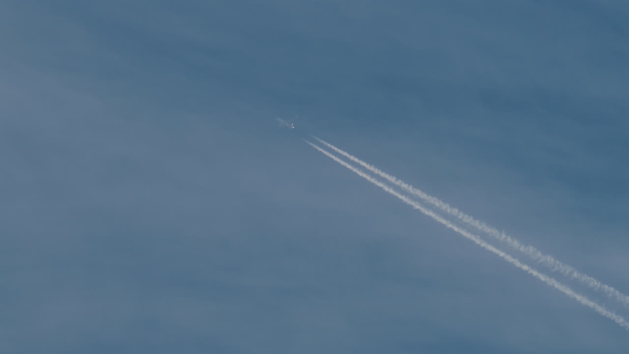 Airplane flying high above leaving long contrails in a clear blue sky
