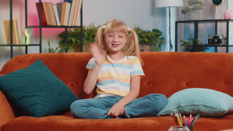 child kid girl smiling friendly at camera waving hands gesturing hello hi greeting at home on couch