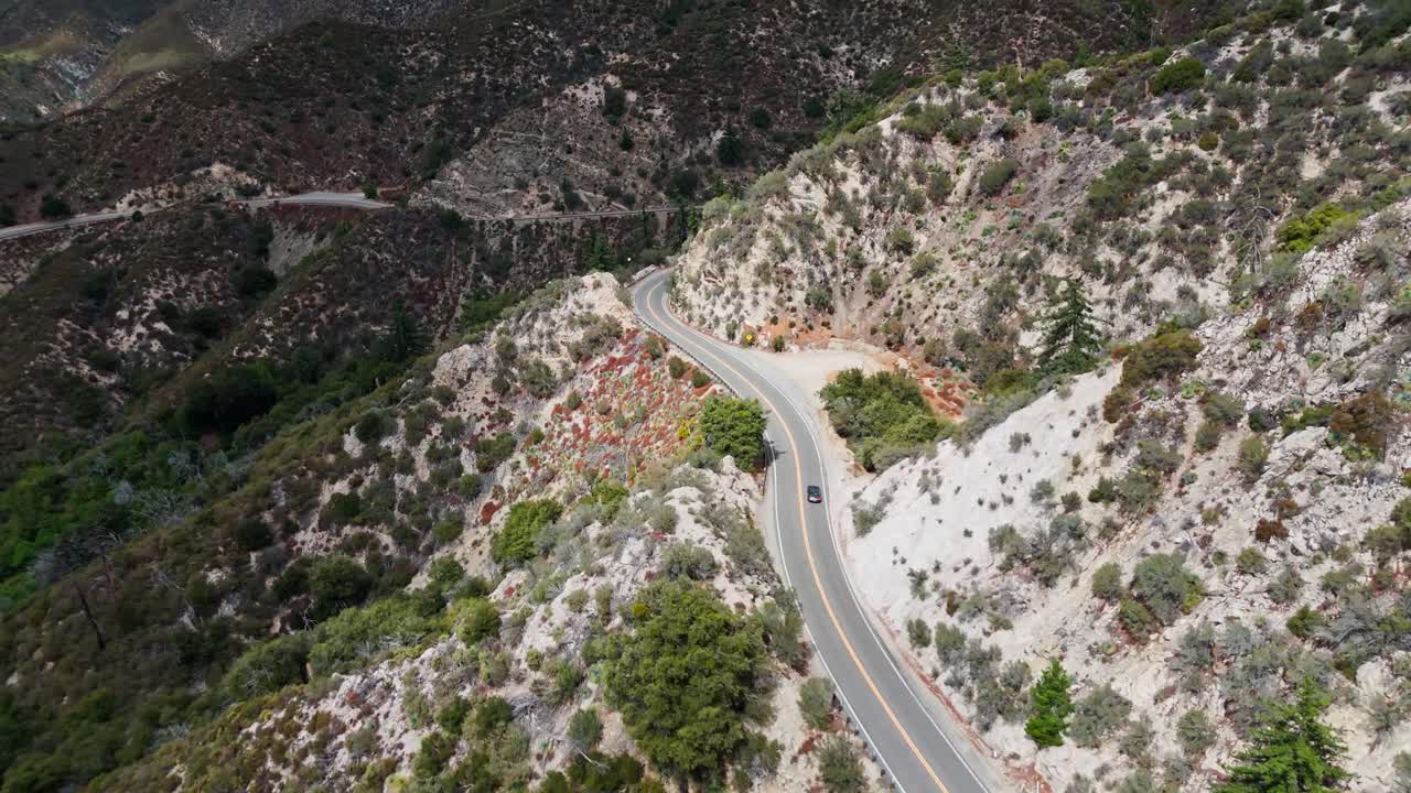 Drone shot of a car driving through the canyons and mountains of Angeles National Forest near LA