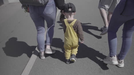 slow motion, single young boy walking, holding mothers hand walking with adult group