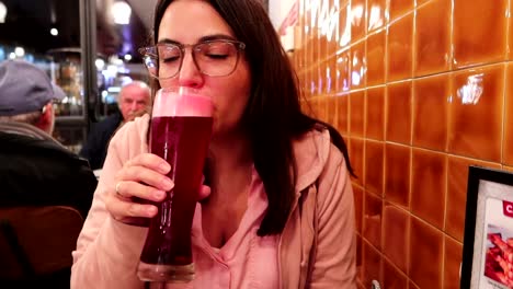 fotografía de una mujer sentada en un pub agarrando un gran vaso de cerveza roja