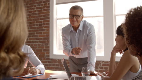 mature businessman standing to address boardroom meeting