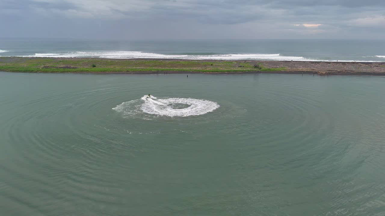 Aerial view a jet ski floats in the calm beach performing circle leaving a trail of white waves behind.
