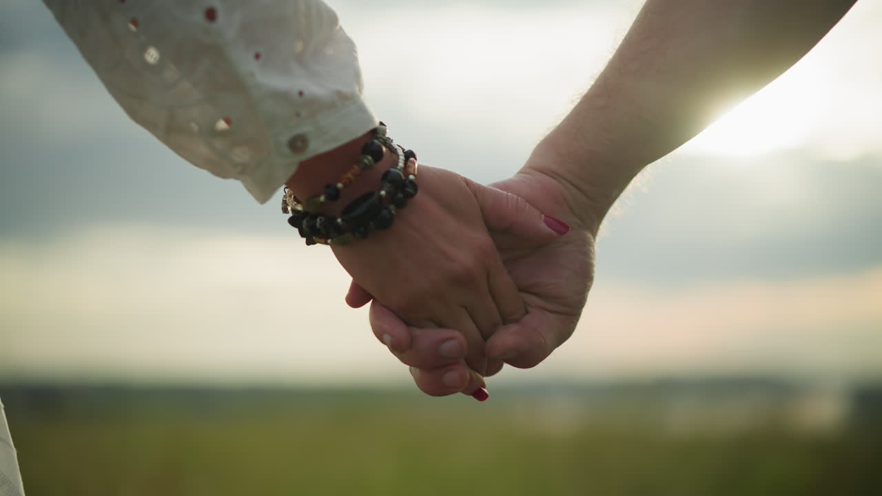 클로즈업 은 두 연인의 손을 잡고 있는 모습으로, 여자의 손은 구슬로 된 팔와 은 손으로 장식되어 있습니다. 태양은 배경에서 부드럽게 빛납니다.