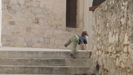 little boy independently climbing up stone rubble stairs, exploring old town by himself