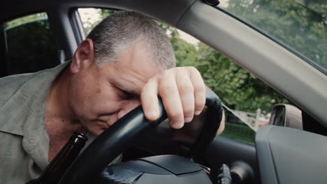 drunk driver with a bottle of alcohol in his hand dozing on the steering wheel