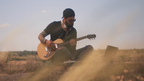 man playing guitar outdoors with laptop