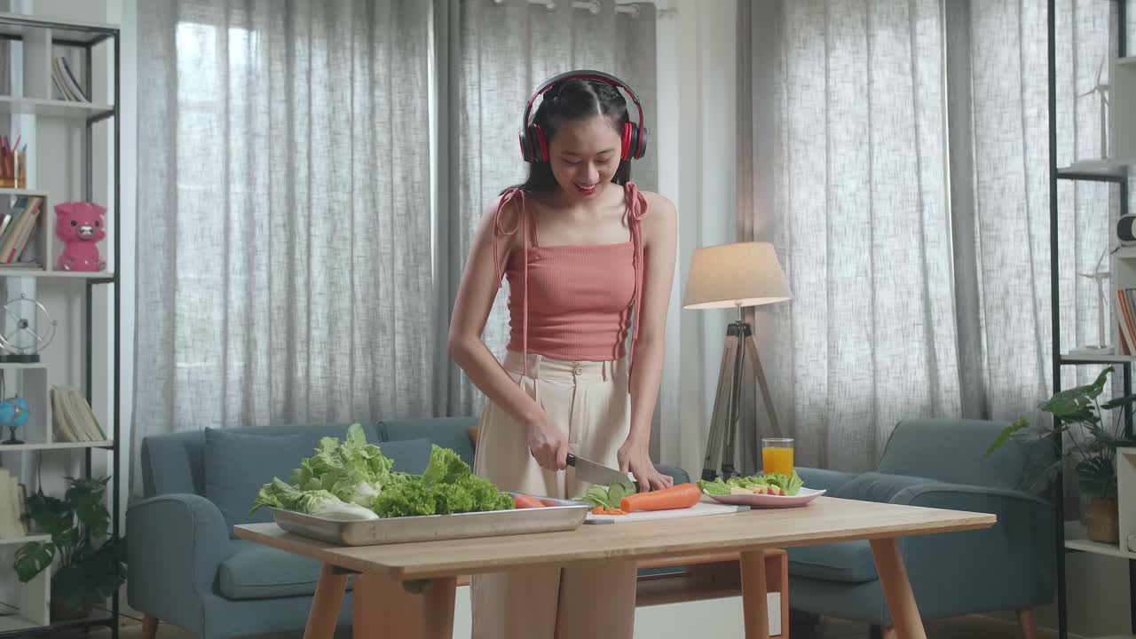 건강한 음식을 먹는 아시아 여성이 헤드폰으로 음악을 듣고 집에서 호박을 는 동안 춤을 추고 있습니다.