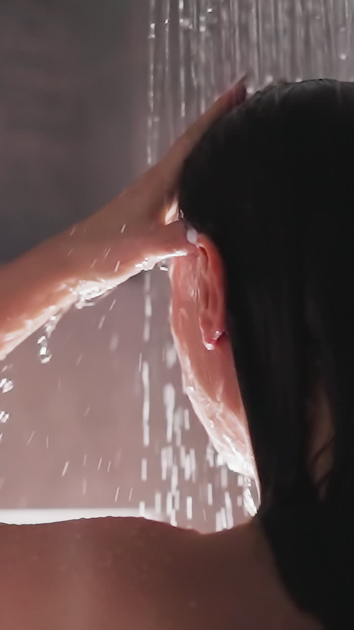 mujer lavando el cabello con champú bajo la ducha contemporánea. dama enjuagando el caballo bajo la ducha moderna en la residencia. morena hace limpieza rutina de lavado de cabello
