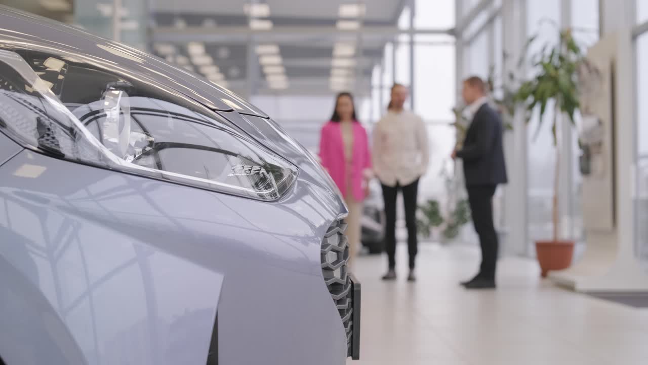 젊은 자동차 판매자가 대리점 살롱에서 젊은 부부에게 새로운 자동차를 보여주고 있습니다.