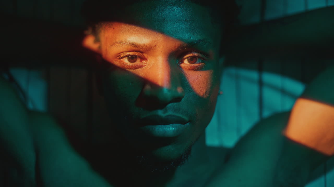 Portrait of Young Black Man Lying on Bed Illuminated by Stripe of Orange Light