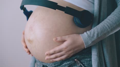 pregnant woman dances with headphones on belly by wall