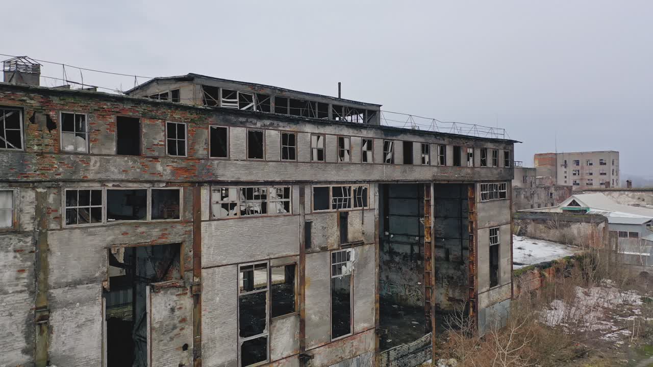 Old abandoned plant with broken windows ruined after the military actions. Demolished plant with pitted roof and some snow on the ground in winter. Aerial view