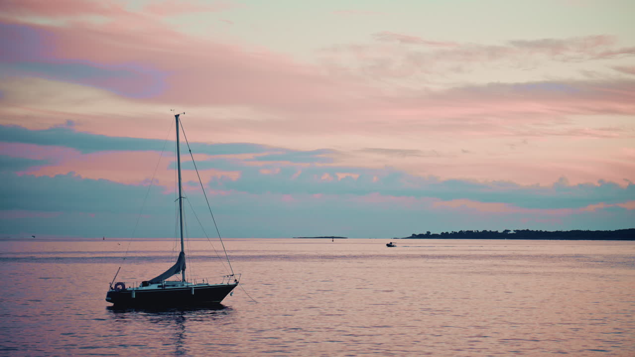A sailboat on calm water during a beautiful pastel sunset