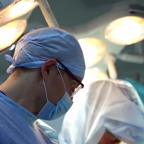 profile view of a doctor. face of a medical male specialist in blue uniform and glasses during the surgery in the operating room.
