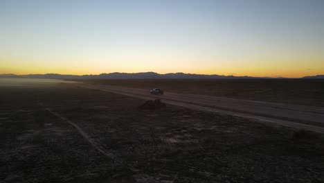 truck driving down a dirt road in the desert as dusk - orbiting aerial view