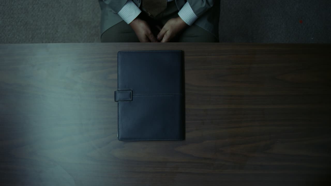 A detective opening and closing a file on a wooden table in an overhead shot.