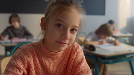 Lindo-Alumno-Sentado-En-El-Escritorio-De-La-Escuela-Primaria.-Niña-Sonriente-Mirando-A-La-Cámara