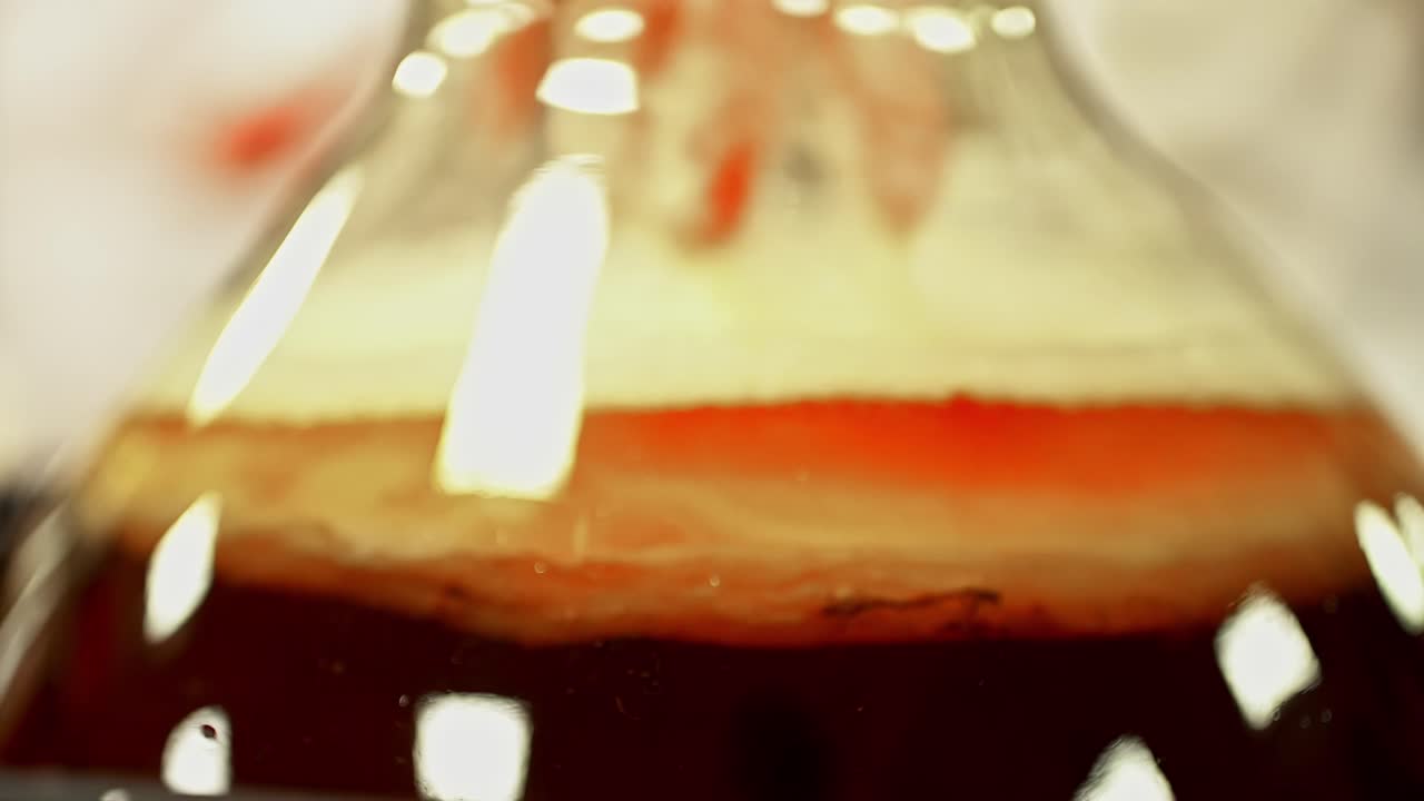 Close up of a gloved hand mixing a red liquid in a glass flask
