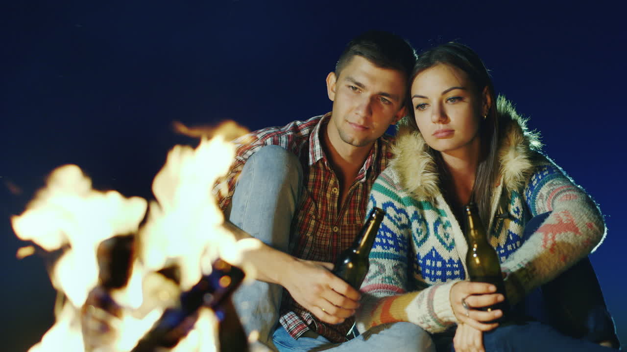 pareja joven relajándose junto al fuego bebiendo una cerveza o una bebida de la botella