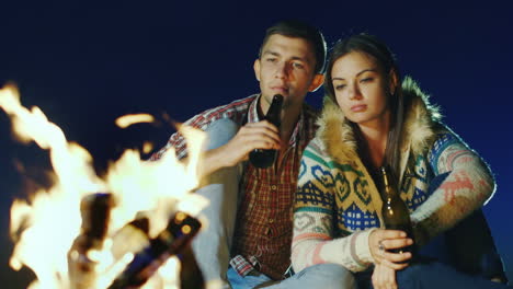 young couple relaxing by the fire drinking a beer or a drink from the bottle